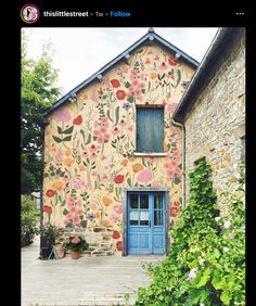 an old building with flowers painted on the side and blue door, in front of it