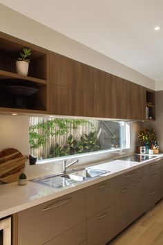 a kitchen with wooden cabinets and white counter tops, plants on the window sill