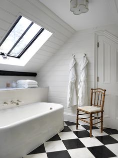 a white bath tub sitting under a window next to a wooden chair and black and white checkered floor