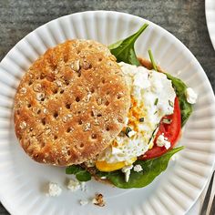 an egg sandwich with spinach and tomatoes on a paper plate next to a fork