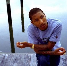 a young man sitting on a dock with his hands in the air and looking at the camera