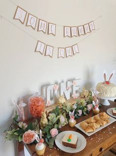 a table filled with desserts and bunnies on top of wooden tables next to a white wall