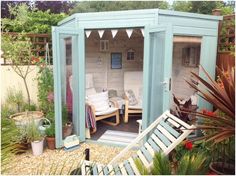 a small garden shed with two chairs and a couch in the back ground, surrounded by plants