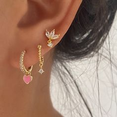 a close up of a person's ear wearing gold earrings with heart and wings