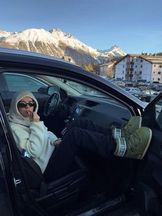 a woman sitting in the passenger seat of a car talking on her cell phone with mountains in the background