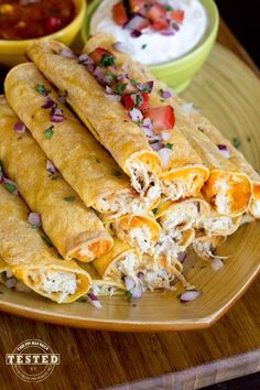 several burritos are stacked on a plate with salsa and sour cream in the background