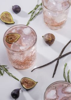 two glasses filled with ice and some figs next to them on a white surface