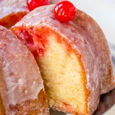 a bunt cake with pink icing and cherries on top is cut in half