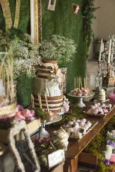 a table topped with lots of desserts next to a wall covered in greenery