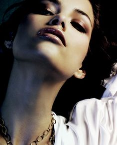 a woman with her eyes closed wearing a white shirt and gold chain necklace, looking up at the sky