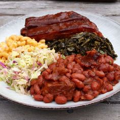 a white plate topped with meat, beans and coleslaw on top of a wooden table