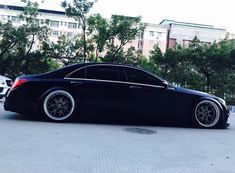 a black car parked on the street next to some trees and buildings in the background