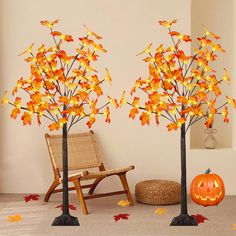 two fake trees with leaves on them next to a chair and pumpkins in the background