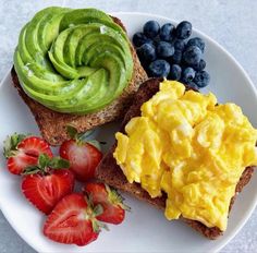 an open face sandwich with avocado, strawberries and blueberries on a white plate