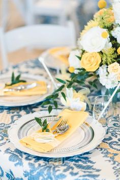 the table is set with yellow and white flowers, silverware, and napkins