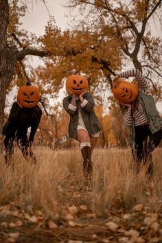 three people wearing pumpkin heads in a field