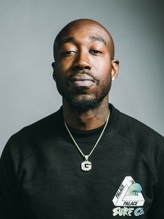 a man with a bald head wearing a black shirt and a gold chain around his neck