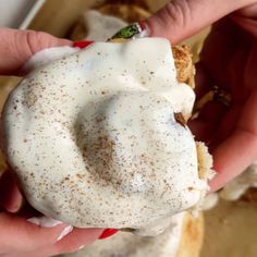 a person holding a doughnut in their hand with white frosting on it and sprinkled with cinnamon