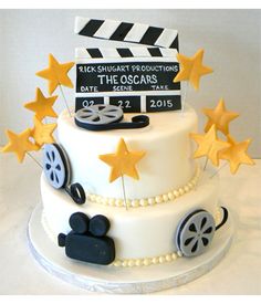 a white cake with black and yellow stars on top is topped with a movie clapper