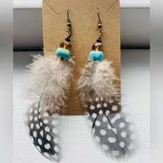 two feathers are hanging from hooks on a card with a brown and blue beaded earring