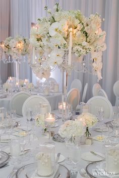 the table is set with white flowers, candles and silverware for an elegant wedding reception