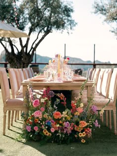 an outdoor table with flowers and candles on it, surrounded by chairs in the grass