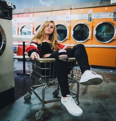 a woman sitting on top of a shopping cart in front of a washer machine