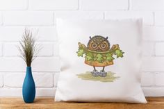 an owl pillow sitting on top of a wooden table next to a blue vase filled with grass