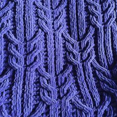 a close up view of a purple knitted sweater with braiding on the sides