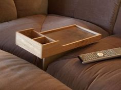 a remote control sitting on top of a brown couch next to a tray with a drawer