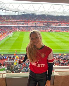 a woman standing in front of a stadium filled with fans and soccer field behind her