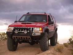 a red four - doored suv parked on top of a dirt hill under a cloudy sky