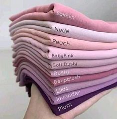 a person holding a stack of pink and purple t - shirts with words on them