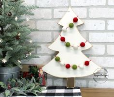 a white christmas tree with red and green balls hanging from it's sides on a wooden stand