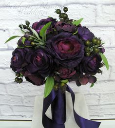 a bouquet of purple flowers in a vase with greenery on the table next to a white brick wall