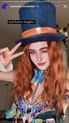 a woman with red hair wearing a blue top hat and holding up her peace sign