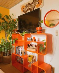 an orange shelving unit in a living room with potted plants and a television