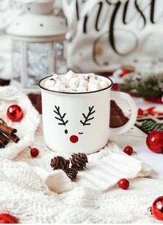 a white mug filled with hot chocolate on top of a table next to christmas decorations