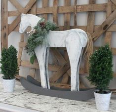 a white horse statue sitting on top of a mantle next to potted plants and pine cones