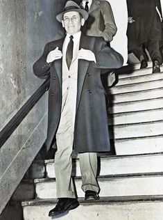 a man in a suit and tie standing at the bottom of stairs with his coat on