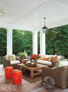 an outdoor living area with wicker furniture and orange accents on the table in front of the couches