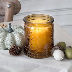 a lit candle sitting on top of a table next to some pine cones and acorns