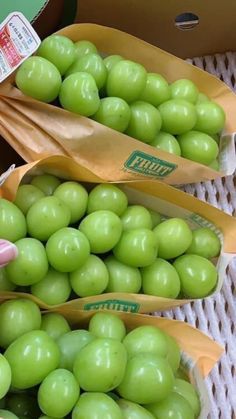 some green grapes are in brown bags on the table and someone is picking them up