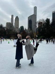 two people standing on an ice rink in the middle of a city with tall buildings behind them