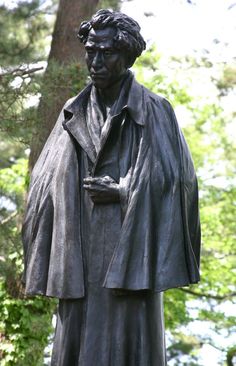 a statue of a man wearing a coat in front of trees