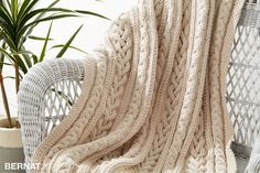 a white wicker chair with a blanket on it and a potted plant next to it