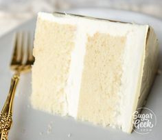 a piece of white cake on a plate with a gold fork next to it,