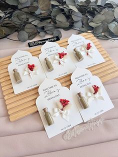 four small bottles with red flowers are sitting on a wooden board next to some leaves