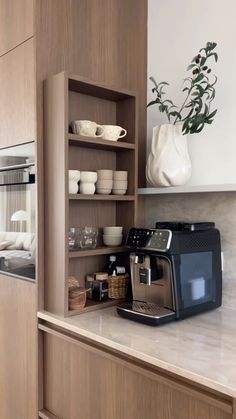 a coffee maker is sitting on the counter in front of a shelf with dishes and cups