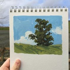 a person holding up a piece of paper with a painting on it that looks like a tree